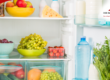 Refrigerator shelf with bowls of grapes, plums, tomatoes, and other fresh produce.