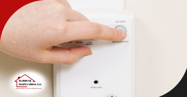 Hand pressing the test/silence button on a smoke detector.