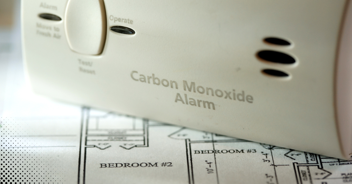 Carbon monoxide alarm sitting on top of a home blueprint.